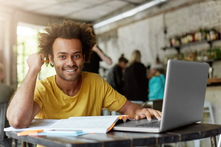  African American college student with cheerful smile using a laptop computer at coffee shop