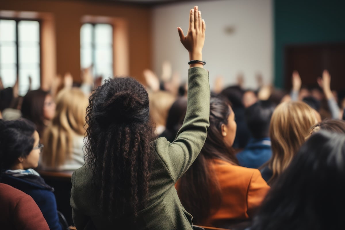 Rear view of black female student raising her hand to ask questions during classroom lecture