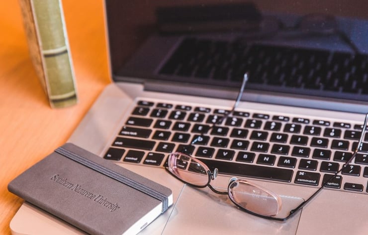 glasses and notebook on top of an open laptop