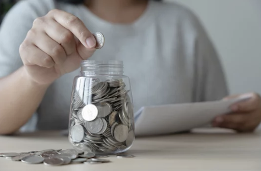 A person placing a coin into a savings jar full of coins. 